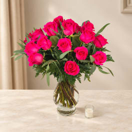 Hot pink roses arranged in a clear glass vase with greenery