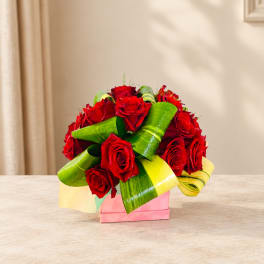 Red roses arranged with bright green leaf wraps in a pink box