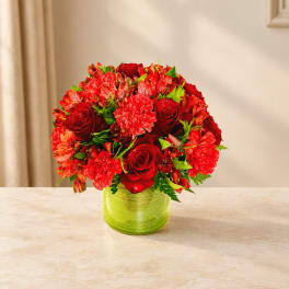 Red roses and mixed red flowers in a green glass vase