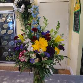 Tall mixed bouquet with yellow gerbera daisies, lilies, and red and purple flowers