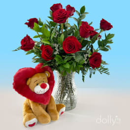 Red roses in a glass vase with a plush teddy bear holding a heart