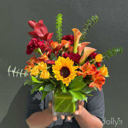 Bright mixed bouquet in a square glass vase with a sunflower and orange blooms