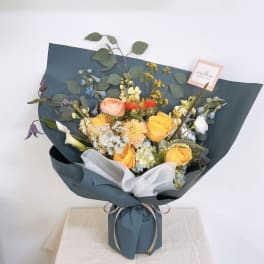 Mixed bouquet of yellow and peach flowers wrapped in dark blue paper
