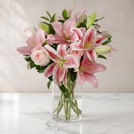 Pink lilies and pale roses arranged in a clear glass vase