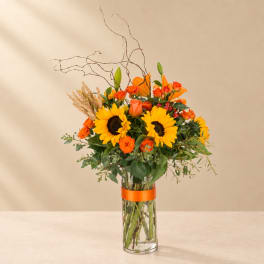 Sunflowers and orange roses in a tall glass vase with branches