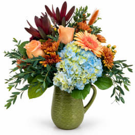 Bouquet of peach roses, blue hydrangeas, and orange mums in a green pitcher