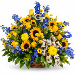 Basket arrangement of yellow roses, sunflowers, and blue flowers with a bee ribbon