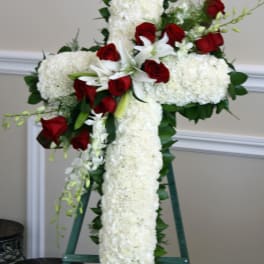White floral cross on an easel with red roses and lilies