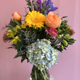 Mixed bouquet in a glass vase with yellow, peach, blue, and purple flowers