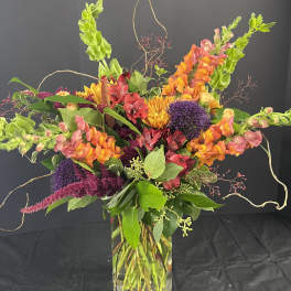 Colorful mixed bouquet in a clear glass vase with orange, pink, purple, and yellow blooms