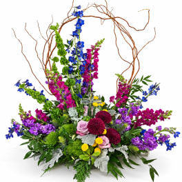 Tall mixed bouquet with blue, purple, pink, and yellow flowers in a low base