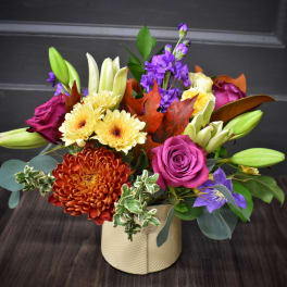 Mixed bouquet in a cream vase with purple, yellow, and orange blooms