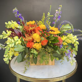 Colorful mixed flower arrangement in a wooden box on a round table