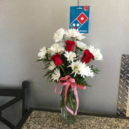 Red roses and white daisies in a clear glass vase with a checkered ribbon.