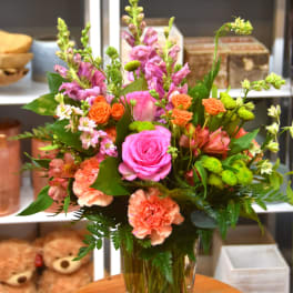 Tall mixed bouquet with pink roses, peach carnations, and orange spray roses in a clear glass vase