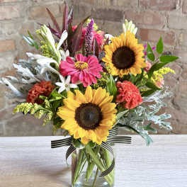Mixed bouquet with sunflowers, pink blooms, and white flowers in a glass vase