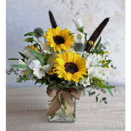 Sunflower arrangement in a clear glass vase with white flowers and a burlap bow