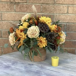 Autumn flower arrangement in a decorative pot with a small yellow candle nearby