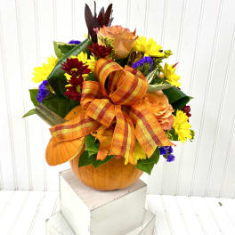 Fall floral arrangement in a pumpkin container with an orange ribbon bow