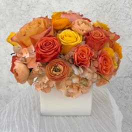 Bouquet of orange, pink, and yellow roses in a white square vase