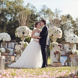 Bride and groom standing among large white and blush floral arrangements outdoors