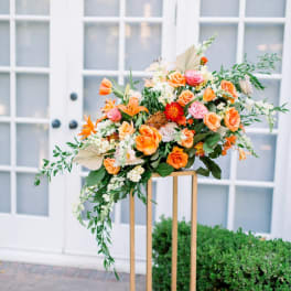 Large orange and pink floral arrangement on a gold stand