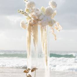 Tall white floral arrangement on a clear pedestal by the beach