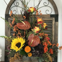 Mixed autumn floral arrangement with sunflowers, roses, and anthuriums in a wooden container