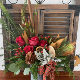 Red roses in a metal vase with pine, pinecones, and a plaid ribbon