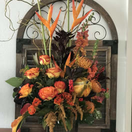 Orange and yellow floral arrangement in a dark vase with tall tropical blooms