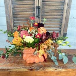 Autumn floral arrangement in a pumpkin-shaped container with orange, pink, and burgundy blooms