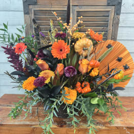 Autumn floral arrangement with orange and purple blooms, pumpkins, and a fan accent