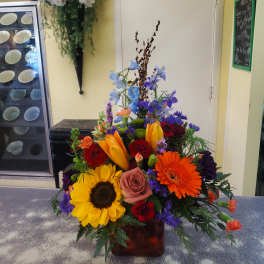 Colorful mixed flower arrangement in a glass vase with sunflowers, roses, and gerbera daisies