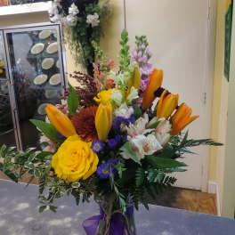 Mixed bouquet with yellow roses, orange lilies, and purple flowers in a vase