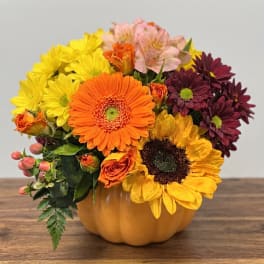 Mixed bouquet in a pumpkin-shaped container with yellow, orange, pink, and burgundy flowers