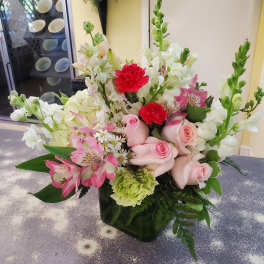 Mixed bouquet of pink roses, white blooms, and red carnations in a square vase