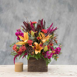 Colorful floral arrangement in a wooden box with a candle beside it