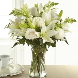 White lilies, roses, and snapdragons arranged in a clear glass vase.
