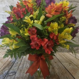 Mixed bouquet of red, yellow, orange, and purple flowers in a glass vase