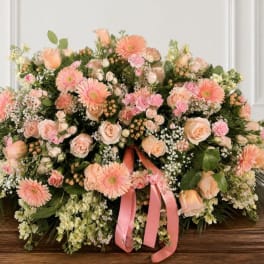 Large peach and pink floral arrangement with a pink ribbon on a wooden table
