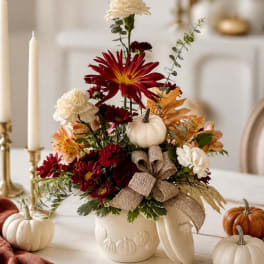 Fall floral arrangement in a white pumpkin vase with a burlap bow