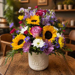 Mixed bouquet with sunflowers, roses, and daisies in a white ceramic jar