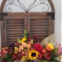 Colorful mixed flower arrangement in a rectangular container with a rustic window backdrop