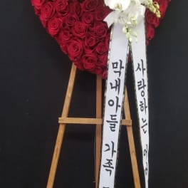 Heart-shaped red rose wreath with white orchids on a wooden stand