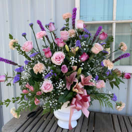 Pink and purple mixed flower arrangement in a white vase with a ribbon