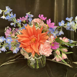 Colorful mixed bouquet in a clear glass vase with orange, pink, and blue flowers
