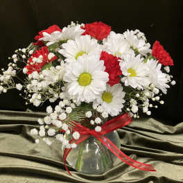 Red carnations and white daisies with baby's breath in a round glass vase with red ribbon