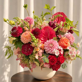 Mixed pink and red flower arrangement in a white bowl vase