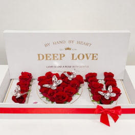 Red roses arranged in a white gift box with butterfly decorations and a red ribbon