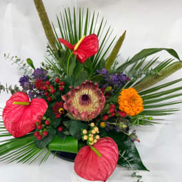 Tropical floral arrangement with red anthuriums, a protea, and orange marigold-like blooms